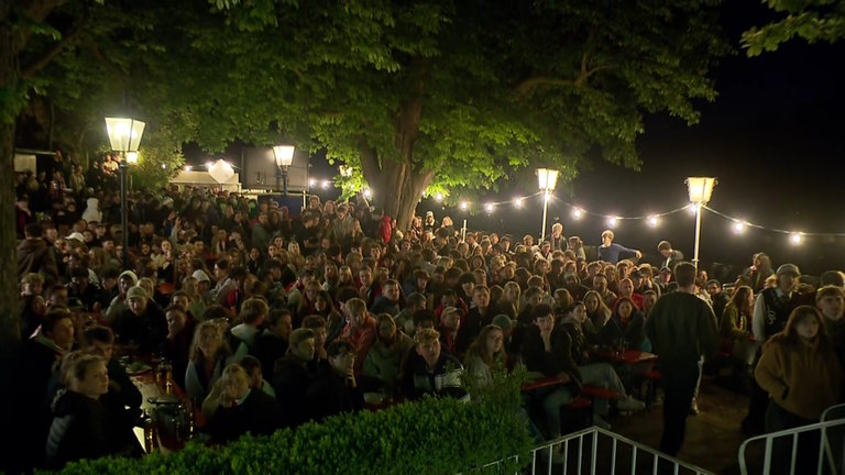 Viele Menschen sitzen an einem Abend in einem Biergarten in Freiburg und schauen ein Fußballspiel.