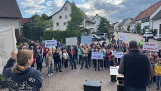 Menschen stehen bei einer Kundgebung und halten Schilder hoch. Wutacher:innen fordern Rücktritt ihres Bürgermeisters.