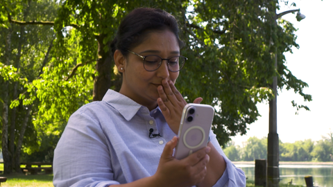 Eine Frau blickt in ihr Smartphone. Ihre Hand berührt ihre Lippen.