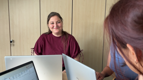 Eine Frau sitzt am Computer und lächelt.