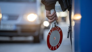 Ein Beamter hält eine Kelle in der linken Hand. 