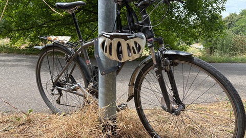 Ein Fahrrad steht abgeschlossen an einer Laterne. An der rechten Seite des Lenkers hängt ein weißer Helm.