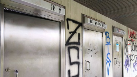 Ein Toilettengebäude an einer Raststätte ist mit Stickern und Graffiti beschmiert. 