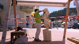 Eine Holzbildhauerin arbeitet beim 29. Holzbildhauersymposium in der Innenstadt von St. Blasien an einer Holzstatue. 