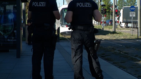 Zwei Polizisten warten an einer Straßenbahnhaltestelle.