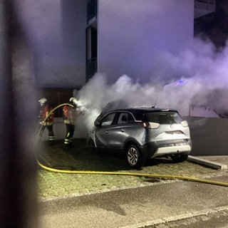 Zwei Feuerwehrleute löschen ein brennendes Auto