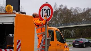 Ein Mitarbeiter der Straßenmeisterei entfernt einen Aufkleber von einem Tempolimitschild. 