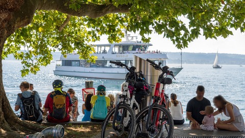 In Überlingen am Bodensee machen Touristinnen und Touristen eine Pause am Wasser. Im Hintergrund ist das Passagierschiff MS Seegold zu sehen.