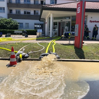 Brauenes Wasser spritzt in einer Fontäne aus gelben Schläuchen, die aus einer Bankfiliale zur Straße ausgelegt sind. Die Feuerwehr pumpt die Filiale der Sparkasse in Oberteuringen aus. 