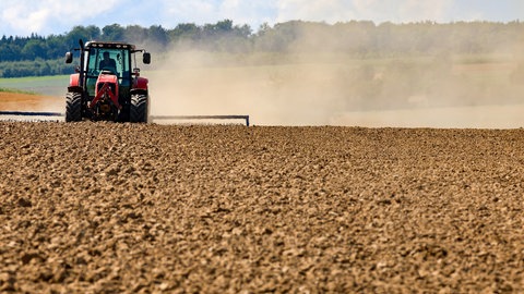 Ein Landwirt bearbeitet ein abgeerntetes Feld und wirbelt dadurch eine Staubwolke auf
