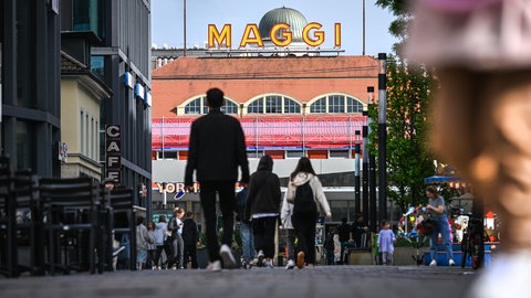 Der Schriftzug MAGGI ist auf einem historischen Gebäude des Unternehmens Maggi angebracht, während im Vordergrund Menschen durch die Innenstadt laufen. 