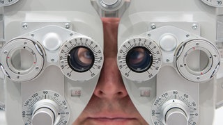 Ein Mann sitzt auf der Optik- und Brillenmesse Opti hinter einem Phoropter.