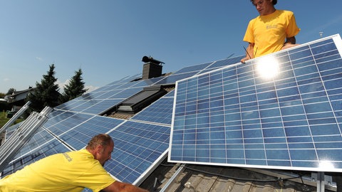 Zwei Handwerker montieren eine Solaranlage auf einem Dach. Interessierte können sich in Konstanz ab sofort auf ein freiwilliges Handwerksjahr im Bereich der Energiewende bewerben.