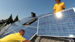 Zwei Handwerker montieren eine Solaranlage auf einem Dach. Interessierte können sich in Konstanz ab sofort auf ein freiwilliges Handwerksjahr im Bereich der Energiewende bewerben.