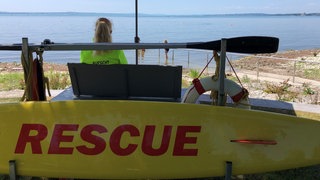 Eine Frau sitzt unter einem Sonnenschirm und blickt auf einen See.