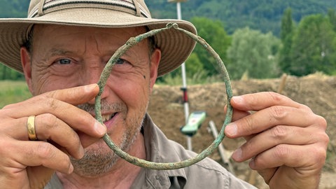 Ein Mann hält einen handtellergroßen Ring aus Bronze.