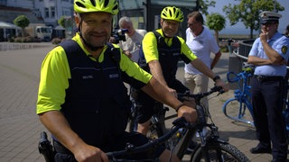 Zwei Polizisten auf Fährrädern in Friedrichshafen schauen in die Kamera