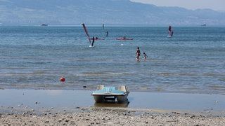 Ein Tretboot liegt an einem Strandbad im seichten Wasser des Bodensees auf Grund. 