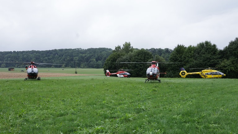 Vier Rettungshubschrauber stehen auf einem Feld nahe des Bahnunglücks. 