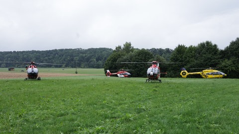 Vier Rettungshubschrauber stehen auf einem Feld nahe des Bahnunglücks. 