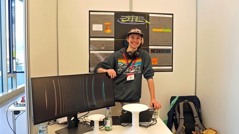 Ein junger Mann steht an einem Schreibtisch mit Monitoren: Der 19-jährige Janosch Homolya vom Schülerforschungszentrum Bad Saulgau hat es geschafft, Wurmlöcher zu visualisieren.