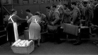Italienische Arbeiter mit Koffern an einem Bahnhof. Im Hintergrund ein Zug. Vor 70 Jahren treffen Deutschland und Italien ein Anwerbeabkommen. In Singen im Kreis Konstanz haben seitdem viele Italiener eine dauerhafte Heimat gefunden und leben bis heute dort.