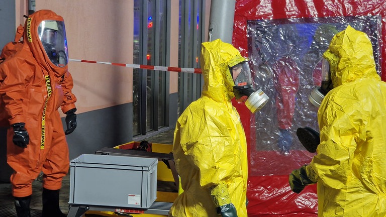 Einsatzkräfte in gelben Schutzanzügen mit Atemschutzmasken stehen im Einsatzbereich in der Konstanzer Innenstadt.