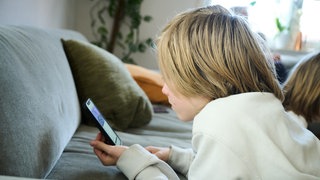 Ein Junge schaut in ein Smartphone (Symbolbild): Immer mehr Kinder haben bereits in der Grundschule ein Handy.