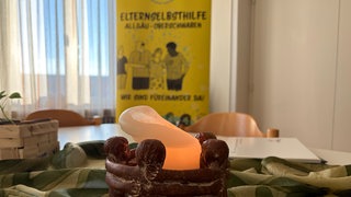 Kerze auf einem Tisch im Raum der Elternselbsthilfe Allgäu-Oberschwaben, im Hintergrund ein Banner der Gruppe. Im Gruppenraum der Elternselbsthilfe Allgäu-Oberschwaben treffen sich Eltern drogenabhängiger Kinder jede Woche.