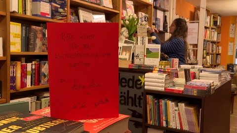 Ein rotes Schild auf einem Büchertisch: Die Ravensburger Buchhändlerin Anna Rahm übt Kritik an Kulturstaatsminister Wolfram Weimer und zeigt ihm symbolisch die "Rote Karte".