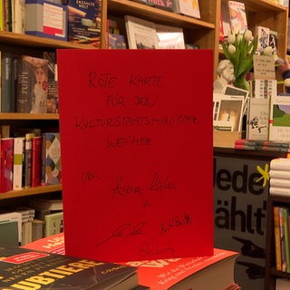 Ein rotes Schild auf einem Büchertisch: Die Ravensburger Buchhändlerin Anna Rahm übt Kritik an Kulturstaatsminister Wolfram Weimer und zeigt ihm symbolisch die "Rote Karte".