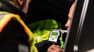 Ein Polizist lässt einen LKW-Fahrer in ein Atemalkoholmessgerät pusten.