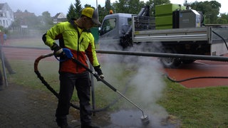 Ein Mitarbeiter einer Gartenbaufirma gießt heißes Wasser auf ein Ameisennest
