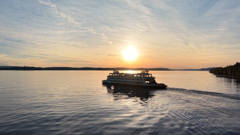 Die Sonne geht hinter der Autofähre auf dem Bodensee auf.