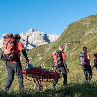 Bergretterinnen und Bergretter aus Vorarlberg laufen mit einer Gebirgstrage zu einem Einsatz.