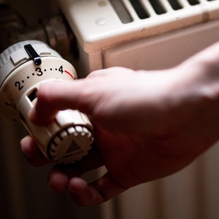 Start der Heizperiode: Eine Person dreht den Thermostat an einem Heizkörper auf. 