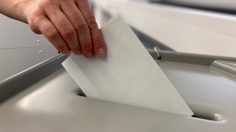 Jemand steckt einen Brief in eine Wahlurne