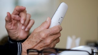 Eine Hand hält ein Telefon. Symbolbild Trickbetrüger.