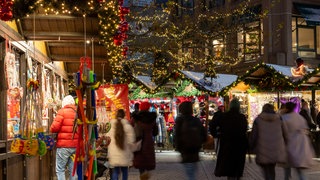 Menschen, unscharf dargestellt, schlendern über den Weihnachtsmarkt in Heilbronn, drum herum beleuchtete Buden