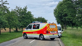 Notarztwagen und weitere Einsatzwagen stehen auf einer gesperrten Straße nach einem Unfall