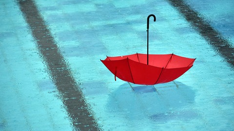  Bei strömendem Regen schwimmt ein Regenschirm im Freibad mit dem Griff nach oben in einem Becken.