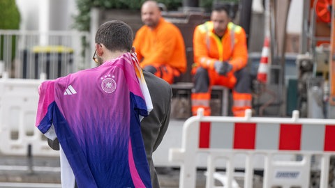 Straßenbauarbeiter beobachten, wie ein Mann mit einem DFB-Trikot entlang läuft