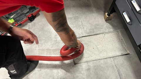 Der Handwerker schließt den Schlauch an die Stutze im Bodenloch an.