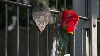 An einem Zaun erinnern ein Herz, eine Rose und eine Kerze an die Verstorbene.
