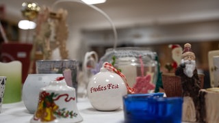 Eine Weihnachtskugel mit der Aufschrift "Frohes Fest" liegt in einem Sozialkaufhaus auf einem Tisch.