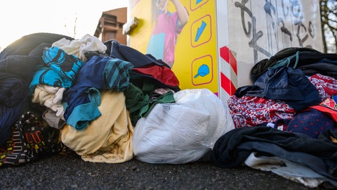 Altkleider vor einem Container (Symbolbild). Immer häufiger landen sehr verschmutzte Textilien im Container. Das treibt die Kosten in die Höhe und macht den Handel nicht mehr rentabel. 