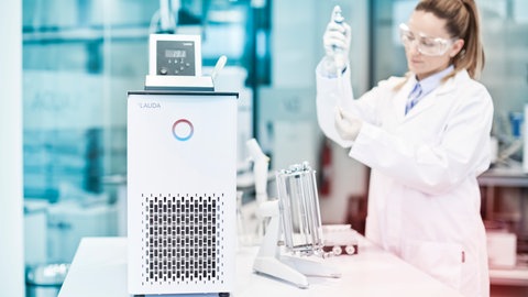Kältethermostat und eine Frau im Laborkittel mit einer Pipette in der Hand. Das Unternehmen LAUDA setzt aktuell auf Kurzarbeit.