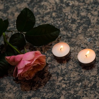 Eine Rose liegt zum stillen Gedenken zwischen Teelichtern. 