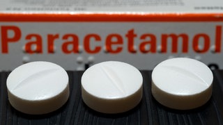 Vor einer Arzneiverpackung liegen Tabletten, die den Wirkstoff Paracetamol enthalten.