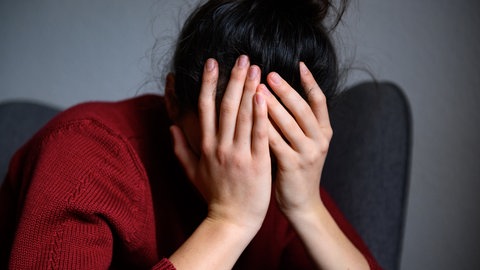 Eine Frau sitzt mit dem Kopf in den Händen auf einem Stuhl. der Weisse Ring berichtet über die Scham der Opfer. (Symbolbild)